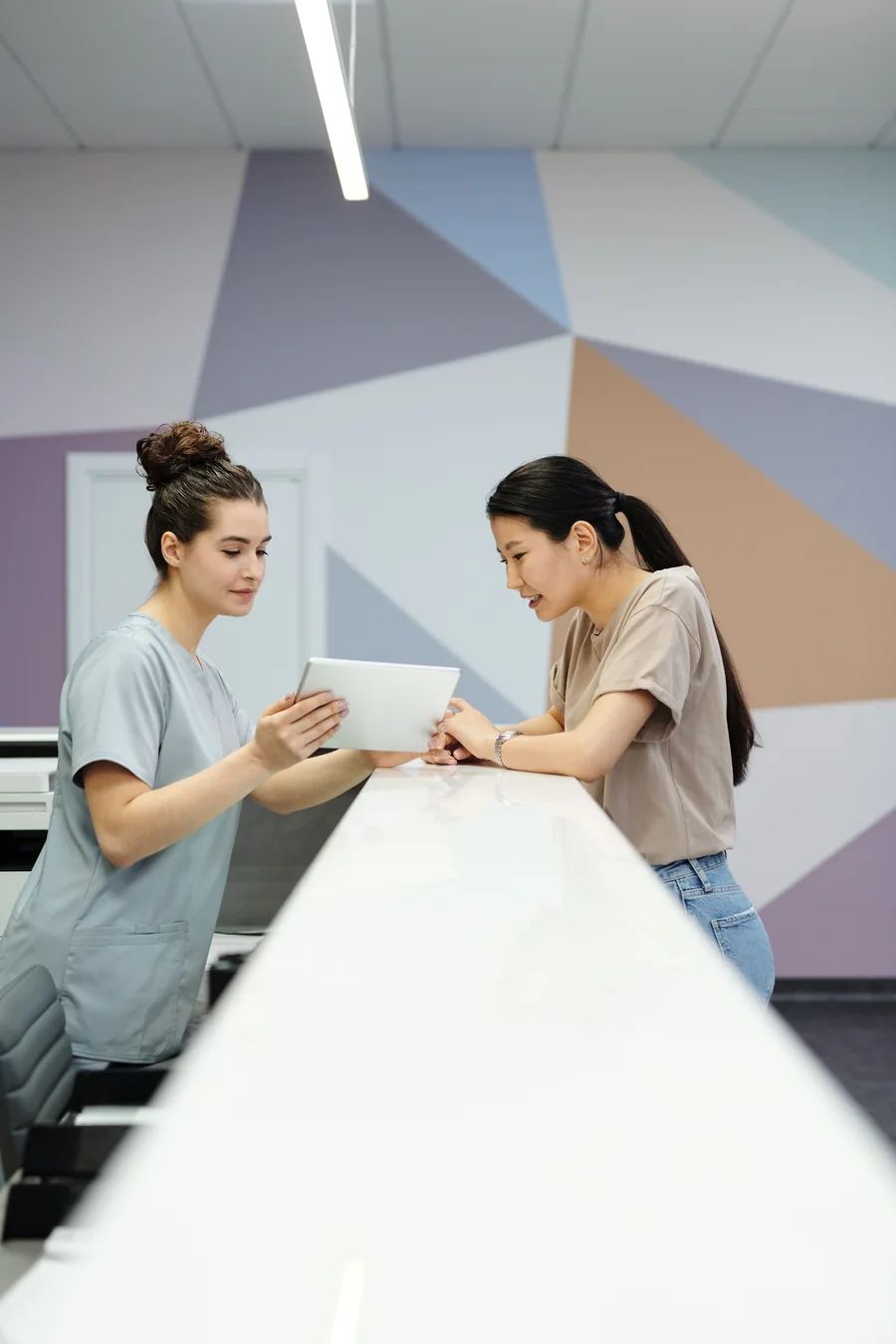 Healthcare worker reviewing information on a tablet with a patient at a reception desk