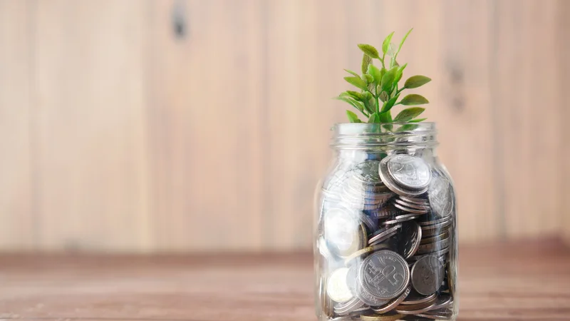 Glass jar filled with coins beside loose coins on a table
