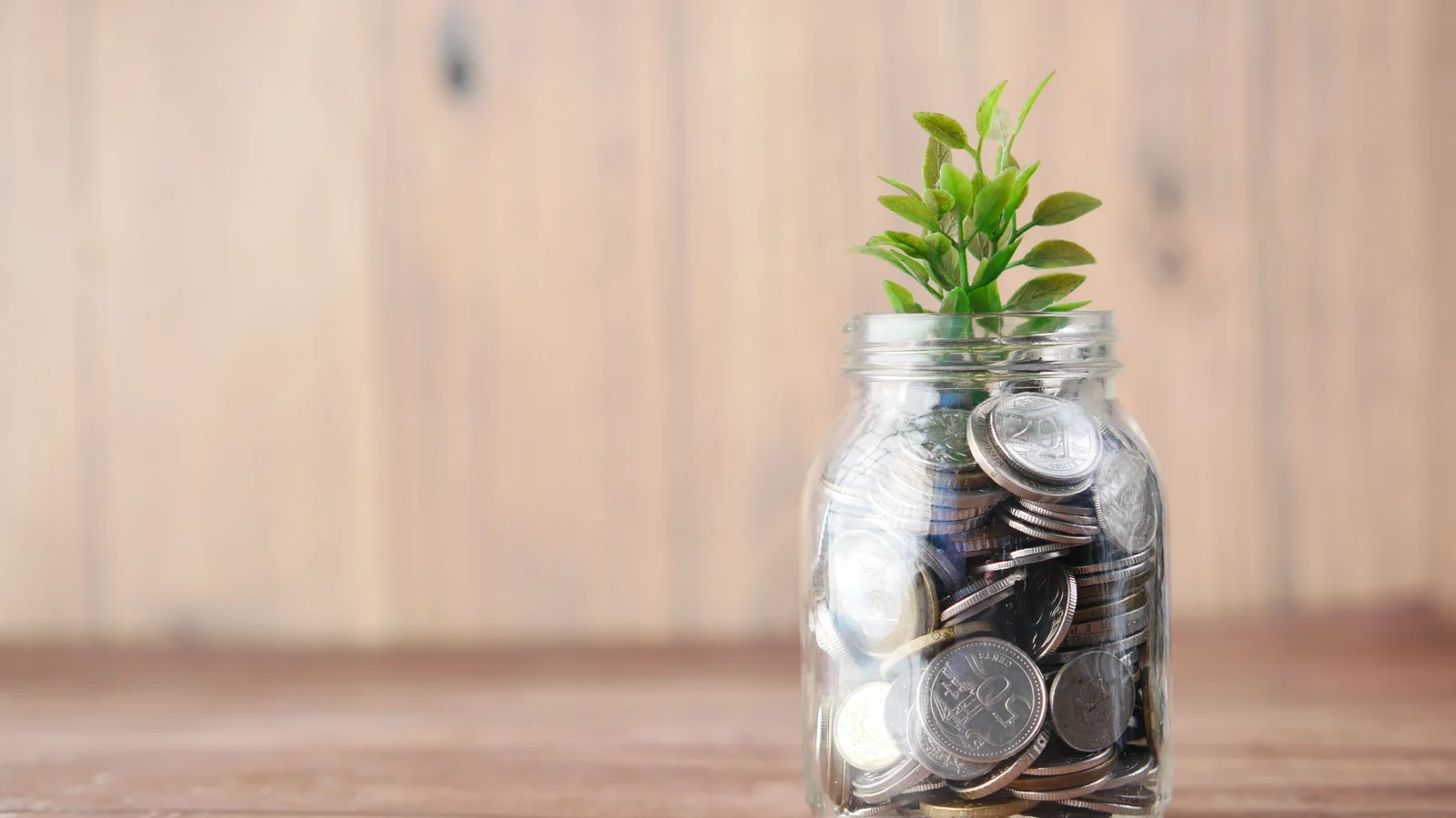 Glass jar filled with coins beside loose coins on a table