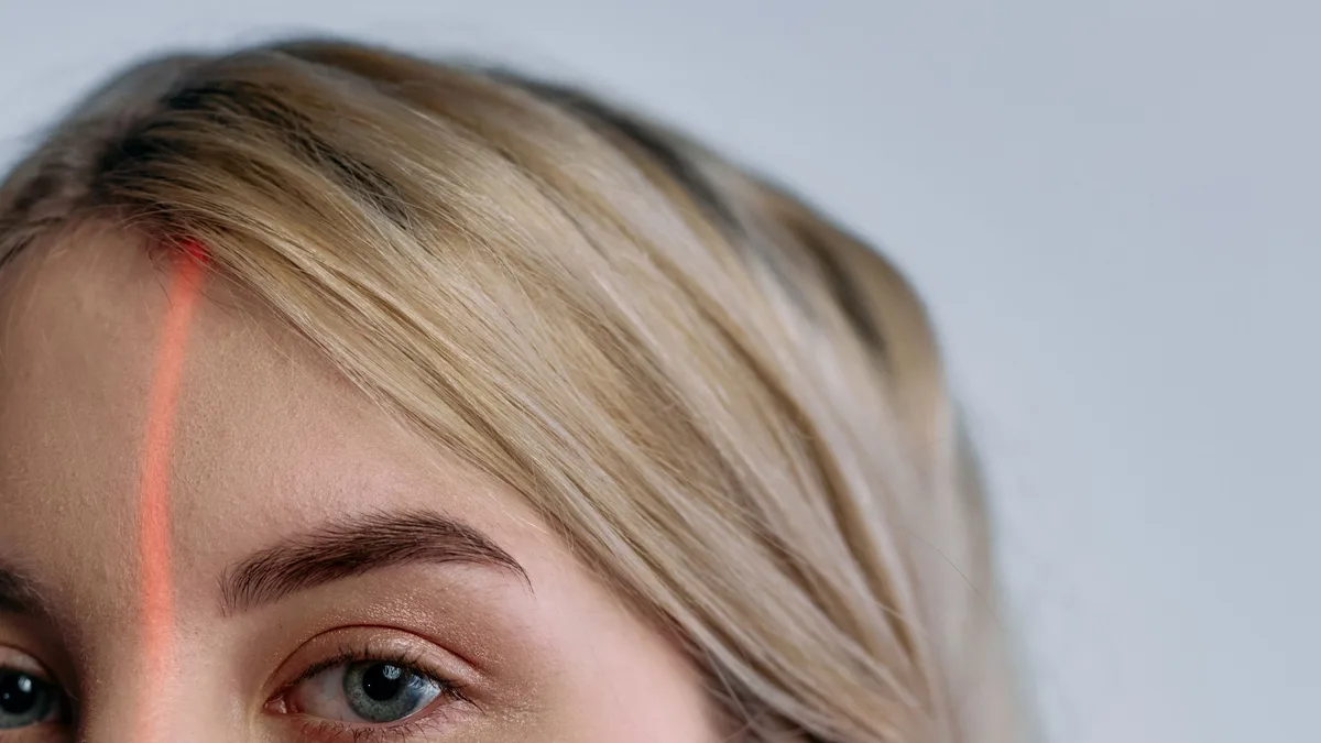 Illustrative portrait crossed by red facial scanning lines, representing synthetic identity and clinician deepfake risk