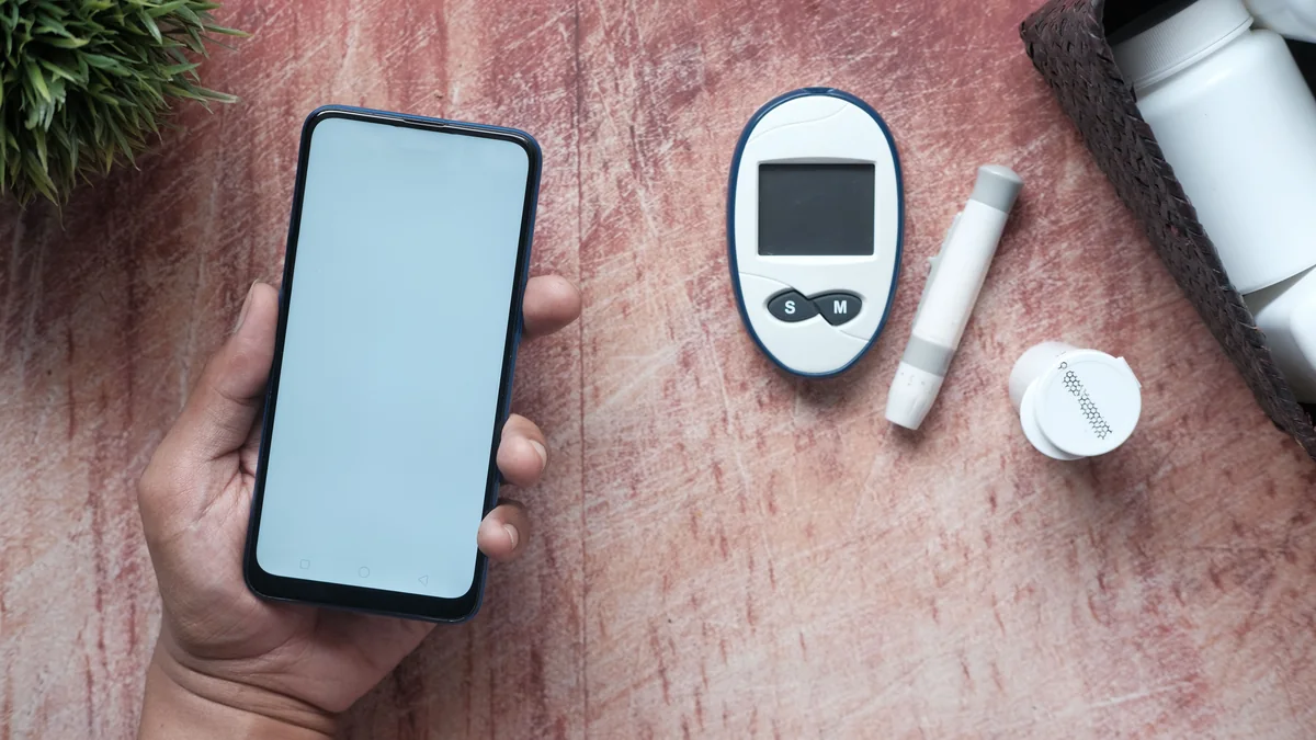 Person holding a smartphone beside glucose monitoring equipment