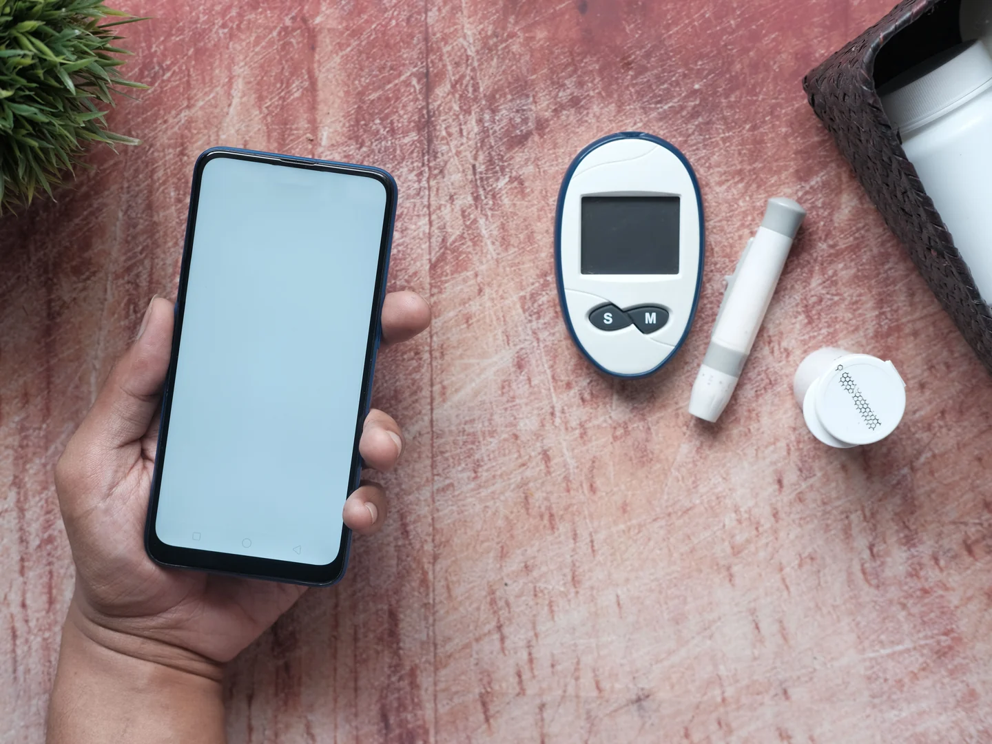 Person holding a smartphone beside glucose monitoring equipment
