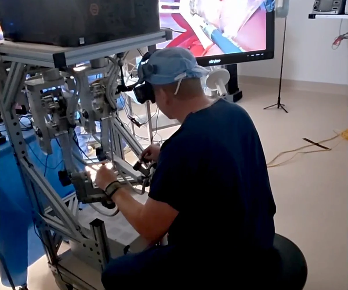Surgeon seated at a teleoperation console while viewing the surgical field on a monitor.